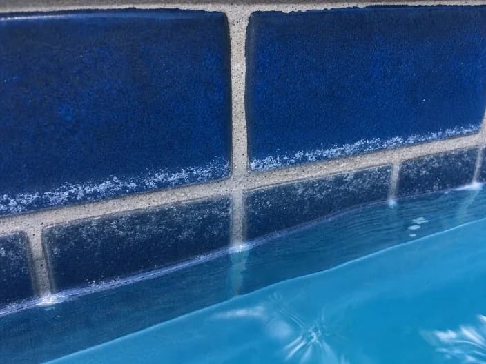 White calcium scale buildup along the waterline tile of a pool, a common result of San Antonio's hard water when water balance is not managed.