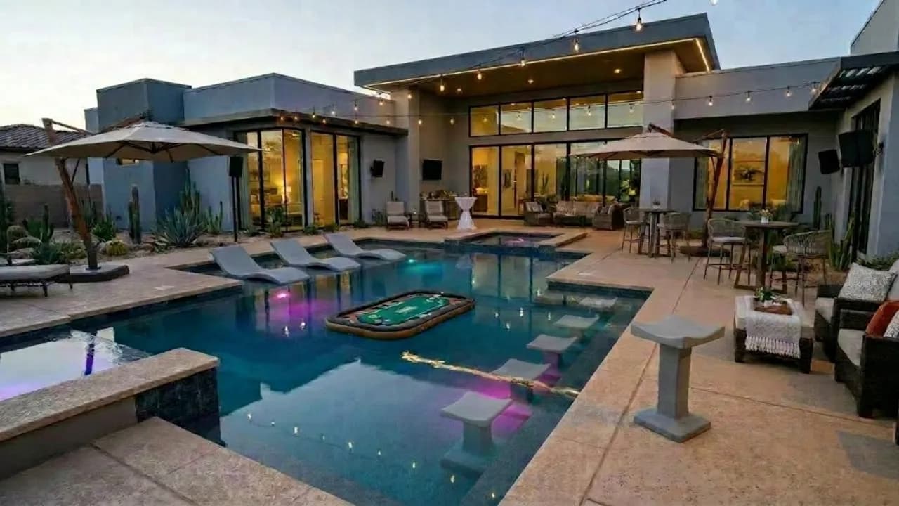 Illuminated luxury backyard pool prepared for an evening event with lounge seating and string lights